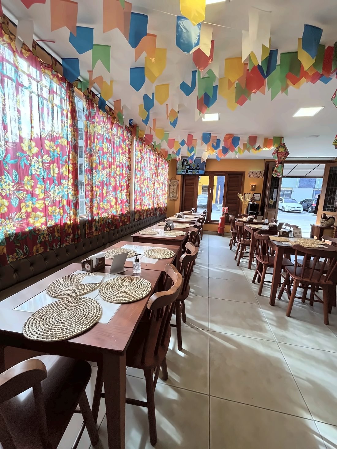 Salão com teto coberto de bandeirinhas coloridas e cortinas de chita nas janelas