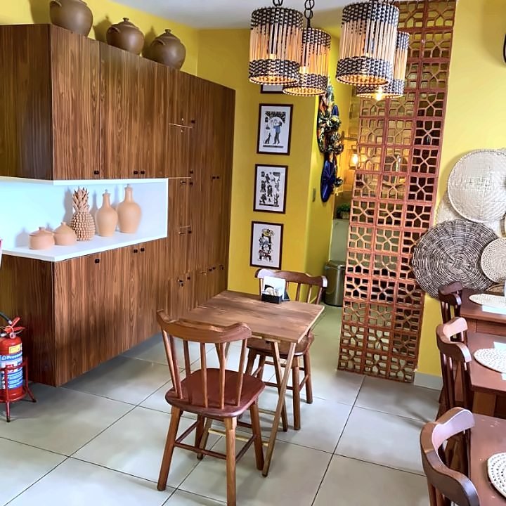 Mesa de madeira ao lado de prateleira com peças de cerâmica e luminárias de palha